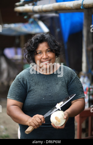 Portrait of smiling Indonesian woman as she prepares a coconut with large knife.  Kupang, West Timor, Indonesia. Nov 2005 Stock Photo