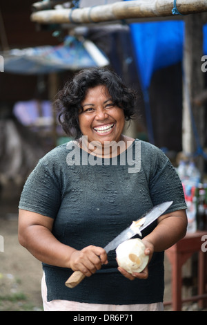 Portrait of smiling Indonesian woman as she prepares a coconut with large knife.  Kupang, West Timor, Indonesia. Nov 2005 Stock Photo
