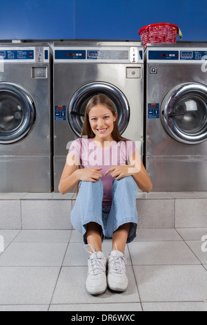 Woman Sitting Against Washing Machines At Laundry Stock Photo