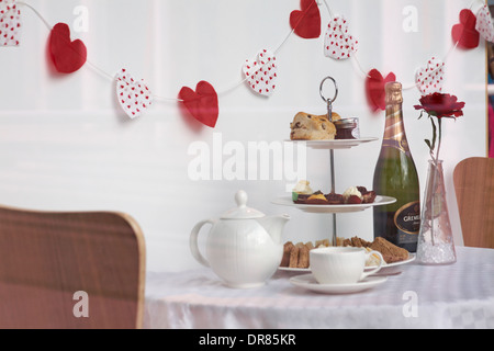 valentine display in window at Portsmouth with tea, bottle of bubbly, stand of cakes and sandwiches, red rose and heart bunting for Valentines day Stock Photo