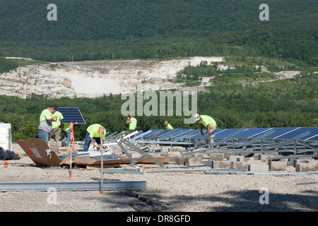 Workers among solar panes near the completion of installation in Adams, Massachusetts.  Working lime pit in background. Stock Photo