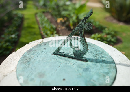 Copper bronze old fashioned sundial on marble pedestal at middad  sunny summer day and flower bed behind Stock Photo