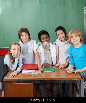 Happy Female Professor With Students At Desk Stock Photo