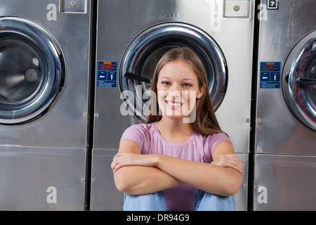 Woman Sitting Against Washing Machines In Laundry Stock Photo