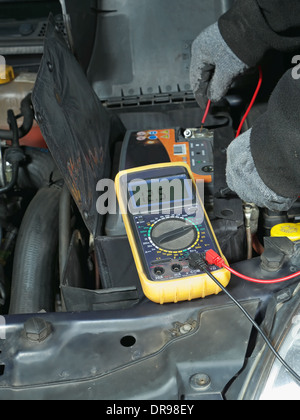 Auto mechanic measuring car battery voltage using multimeter Stock Photo