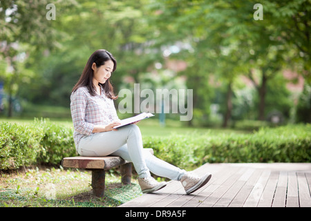 a woman sitting on a bench reading a book Stock Photo