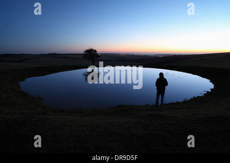 Man contemplating the meaning of life by a dew pond on the South Downs at dusk. Stock Photo