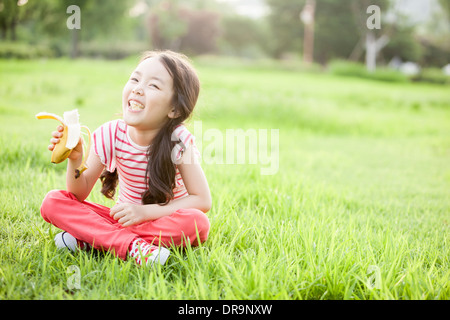 a girl sitting on the grass eating a banana Stock Photo