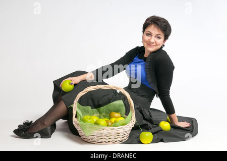 Young female with green apples and a basket sitting on a white background in studio Stock Photo