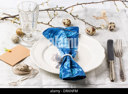 Easter table setting with vintage silverware, white plate, gray textile napkin, quail eggs and blossom branch on old wood Stock Photo