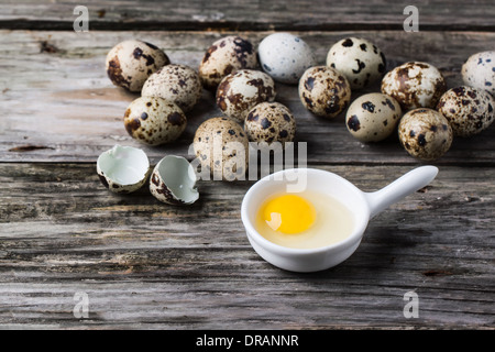 Whole and broken quail eggs and yolk in white bowl over old wooden background Stock Photo