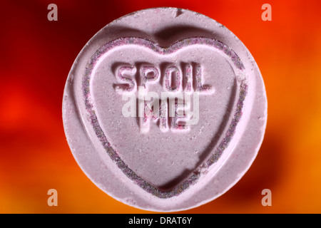 Love heart sweets with spoil me message on artificial rose petals Stock Photo
