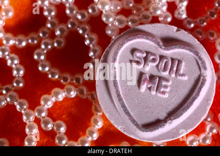 Love heart sweets with spoil me message placed on hearts and artificial rose petals Stock Photo