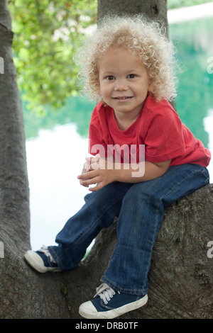 Portrait of happy little boy sitting on tree Stock Photo