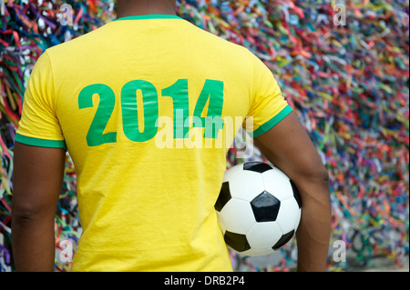 Brazil 2014 soccer player standing with football in front of wall of colorful lembranca wish ribbons in Salvador Bahia Brazil Stock Photo