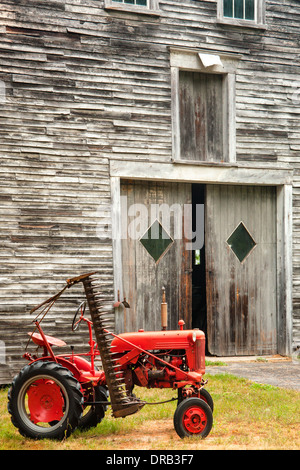 An antique red International Cub Low Boy tractor sitting in front of an old wooden barn. Stock Photo