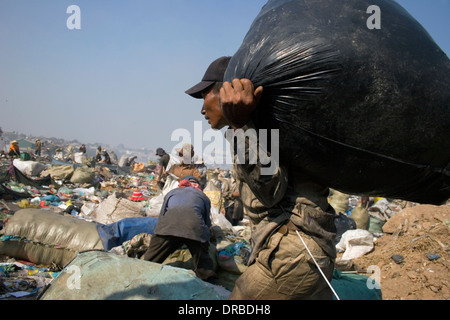 A man who is a scavenger worker is carrying a large sack filled with garbage at the Stung Meanchey Landfill in Phnom Penh, Cambo Stock Photo