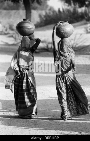 Woman women in ghunghat veil balancing water pots on head Udaipur Rajasthan India Asia Indian Asian 1976 old vintage 1900s picture Stock Photo