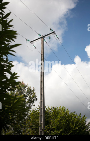 Telegraph pole with 3 wires  in France against blue summer sky with white clouds and lush green foliage of trees. Stock Photo