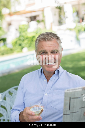 Senior man reading newspaper and drinking wine in backyard Stock Photo