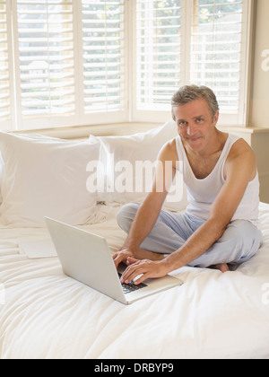 Man using laptop on bed Stock Photo