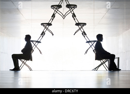 Businessmen sitting at opposite ends of office chair installation art Stock Photo