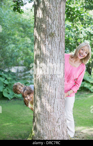 Grandmother and grandchildren peering behind tree Stock Photo