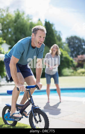 Man riding small bicycle at poolside Stock Photo