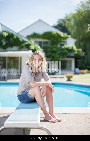 Woman sitting on diving board at poolside Stock Photo