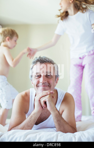 Children jumping on bed around father Stock Photo