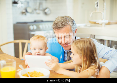 Father and children using digital tablet at table Stock Photo
