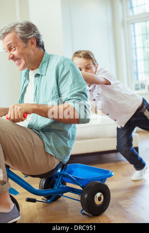 Boy pushing father on tricycle indoors Stock Photo