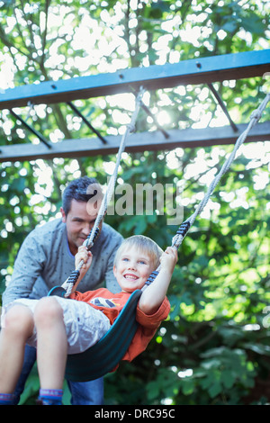 Father pushing son on swing outdoors Stock Photo