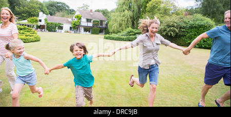 Multi-generation family holding hands and running in backyard Stock Photo