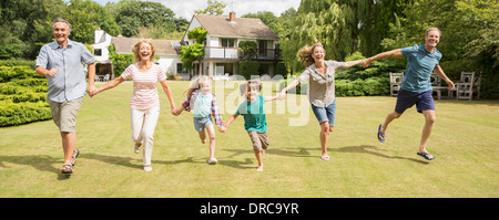 Multi-generation family holding hands and running in grass Stock Photo