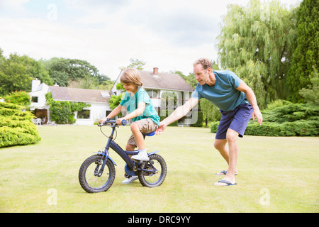 Father pushing son on bicycle in backyard Stock Photo
