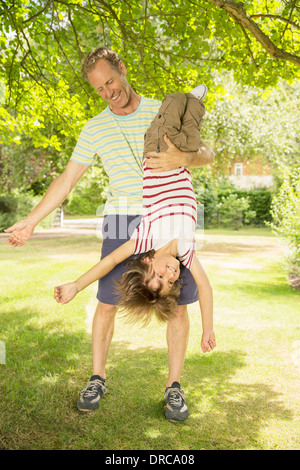 Father holding son upside-down in backyard Stock Photo