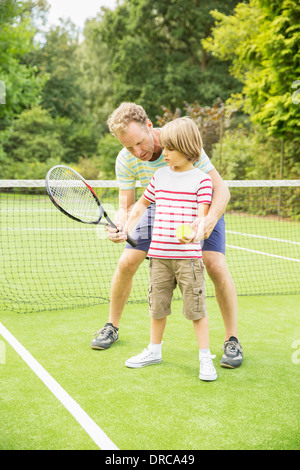 Father teaching son to play tennis on grass court Stock Photo