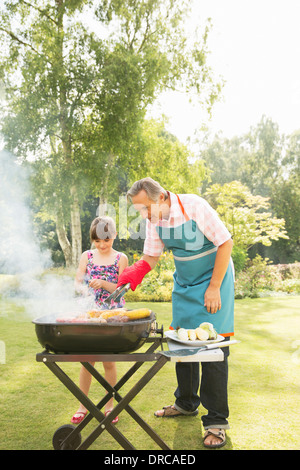 Grandfather and granddaughter grilling at barbecue in backyard Stock Photo