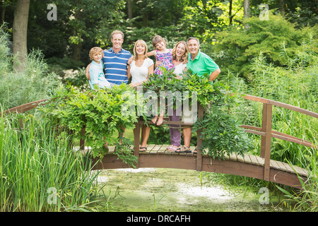 Multi-generation family standing on wooden footbridge over pond Stock Photo