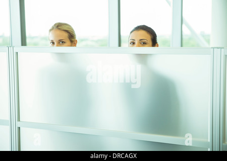 Businesswomen peeking over half wall in office Stock Photo