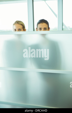 Businesswomen peeking over half wall in office Stock Photo