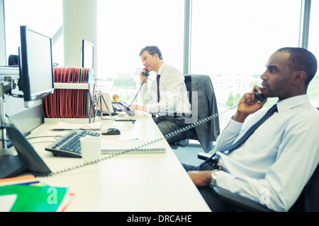 Businessmen talking on telephones in office Stock Photo
