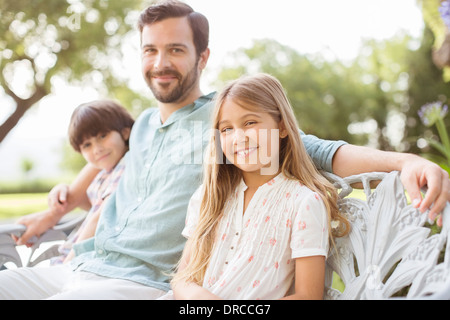 Father and children smiling on bench Stock Photo