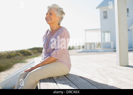 Senior woman sitting on deck outside beach house Stock Photo