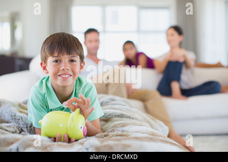 Boy with piggy bank on sofa in living room Stock Photo