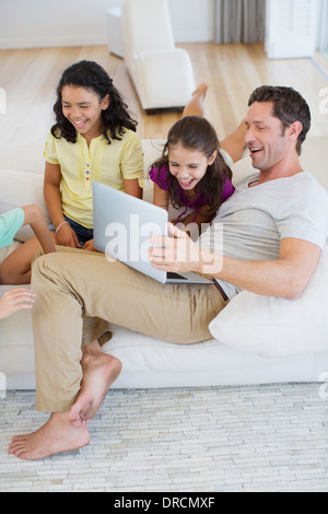 Father and daughters using laptop on sofa in living room Stock Photo