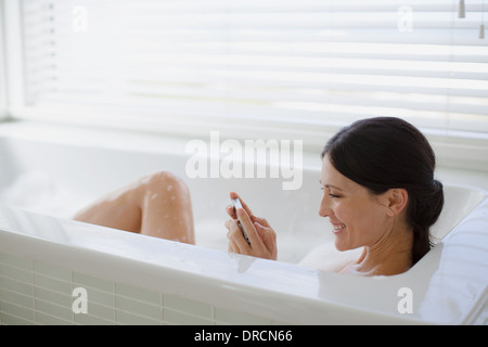 Woman using cell phone in bubble bath Stock Photo