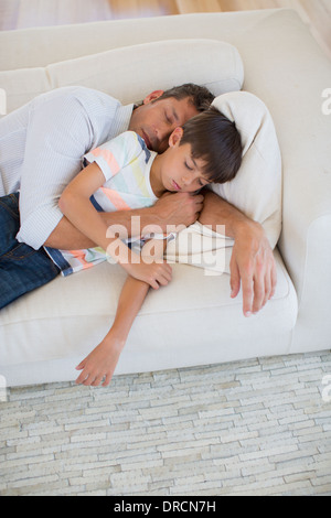 Father and son napping on sofa in living room Stock Photo