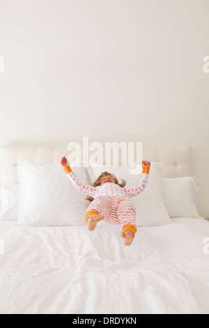 Girl in colorful jammies jumping on bed Stock Photo